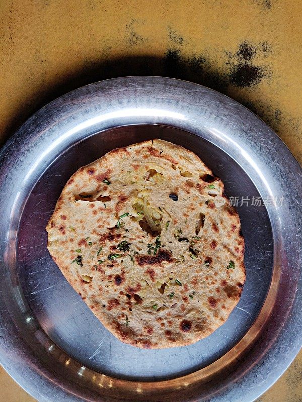 Amritsari Aloo-Paratha，库尔查塞满了土豆，洋葱，绿色丹尼亚和香料，盛在一个钢板或塔利放在一个木制表面。